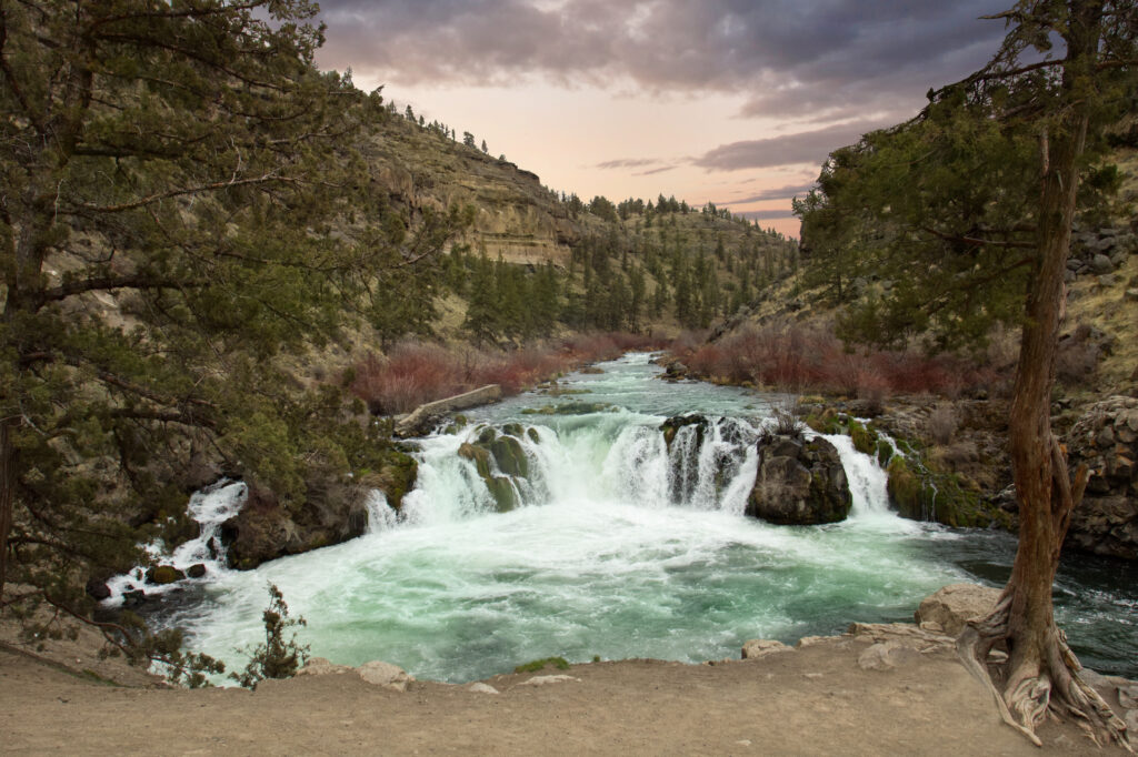 Tranquil river flowing into vibrant waterfall with lush trees rugged mountains scenic wallpaper