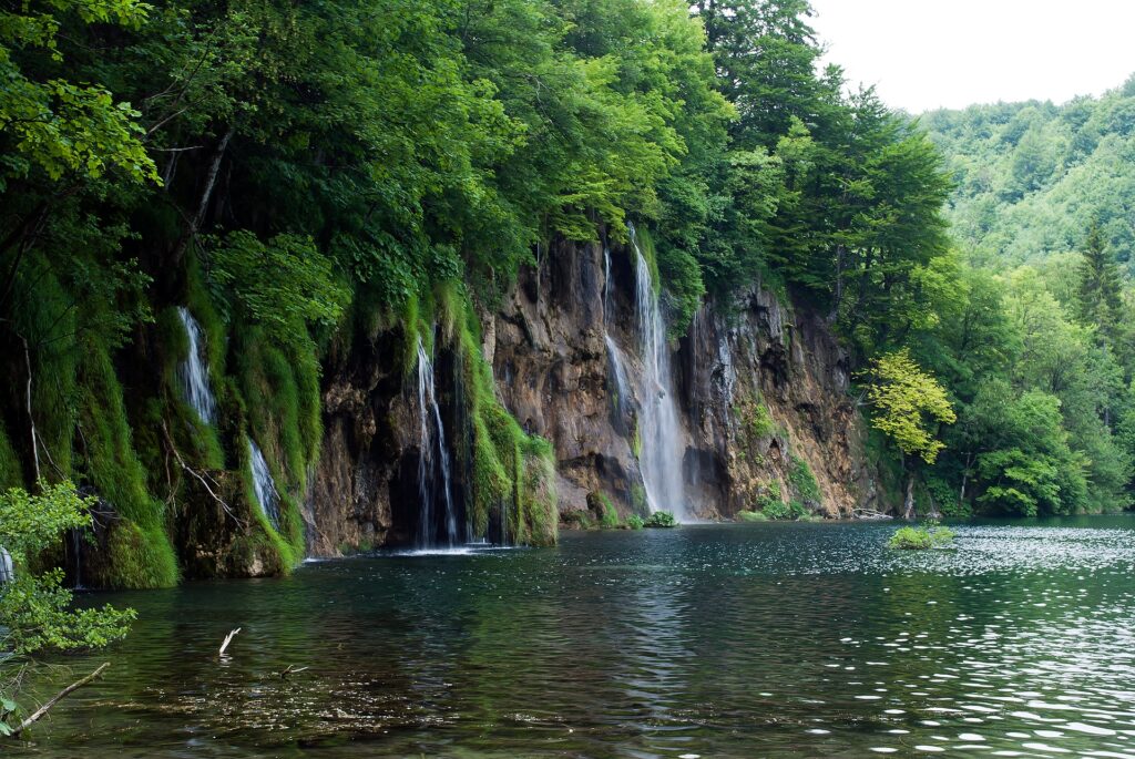 Tranquil river with lush green trees and cascading waterfalls by dramatic cliffs wallpaper background