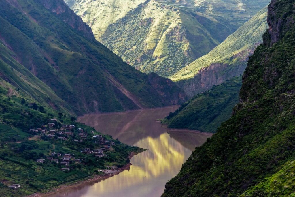 Aerial view of river winding through green mountains with village capturing serene rural landscape Wallpaper