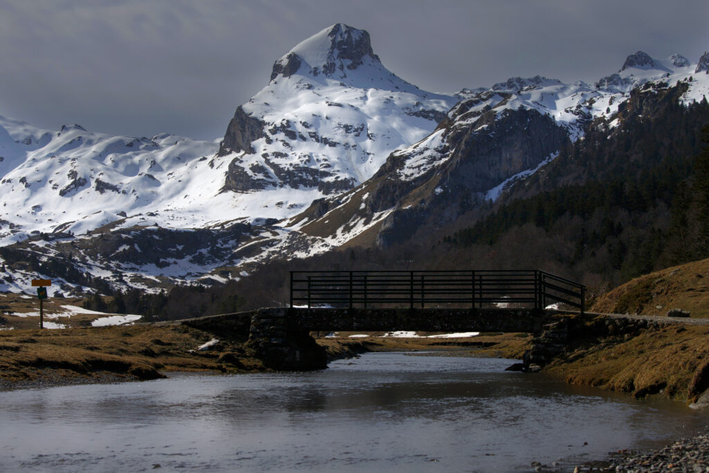 Tranquil river under rustic bridge with snow-capped mountains peaceful nature wallpaper background