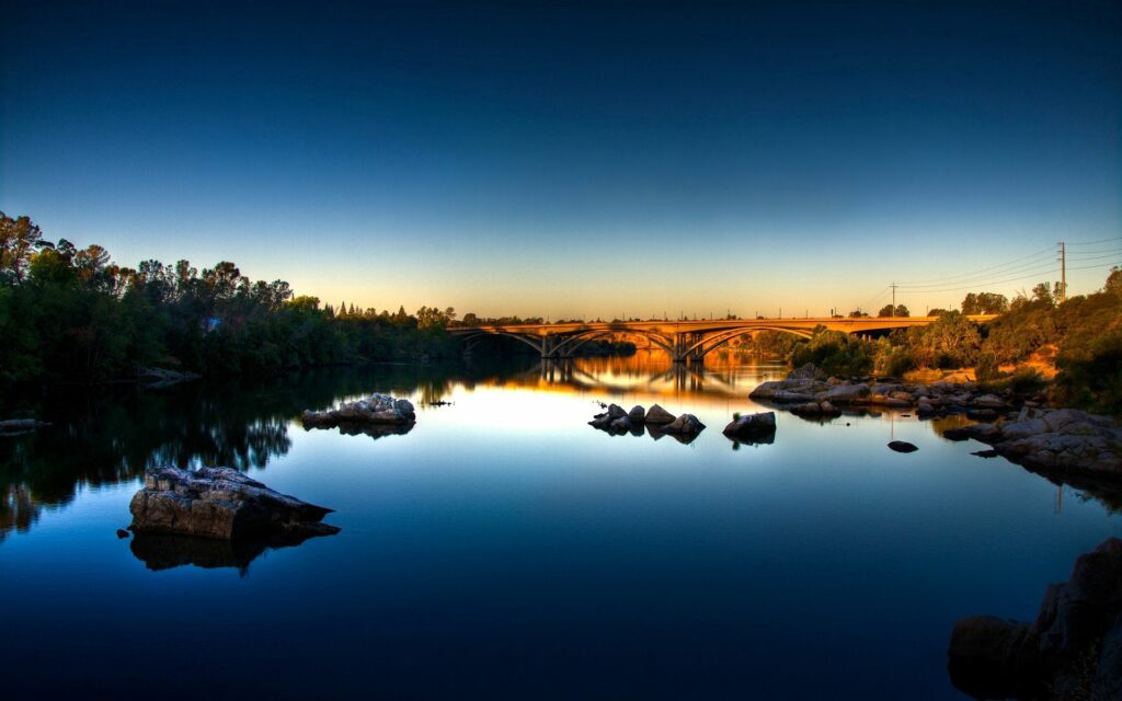 Tranquil dawn river wallpaper with smooth water stones graceful bridge and soft blue tones