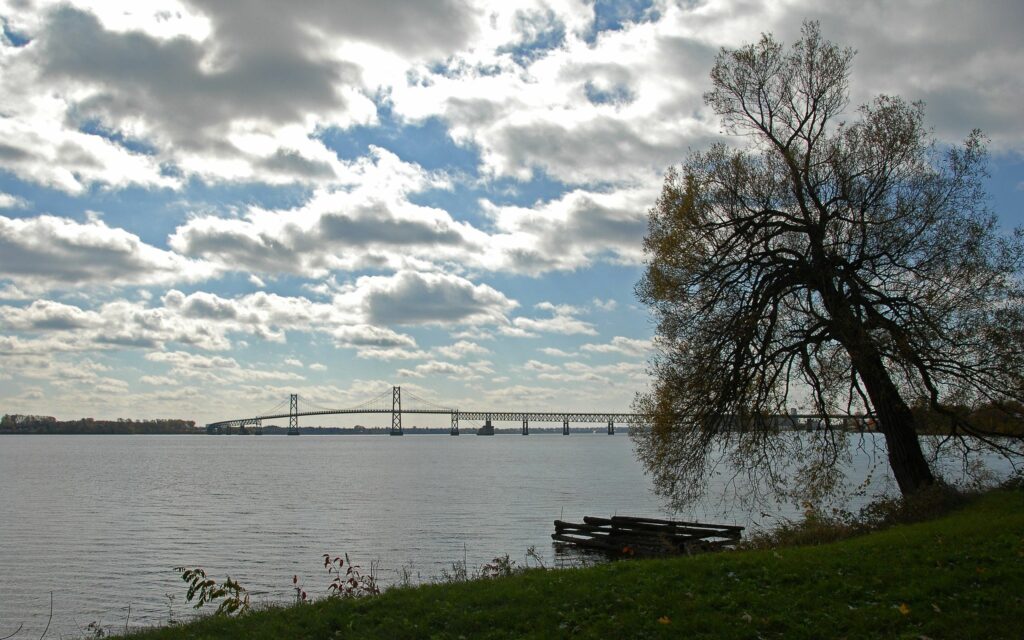 Serene riverside with graceful bridge lush grass calm water soft scattered clouds scenic wallpaper