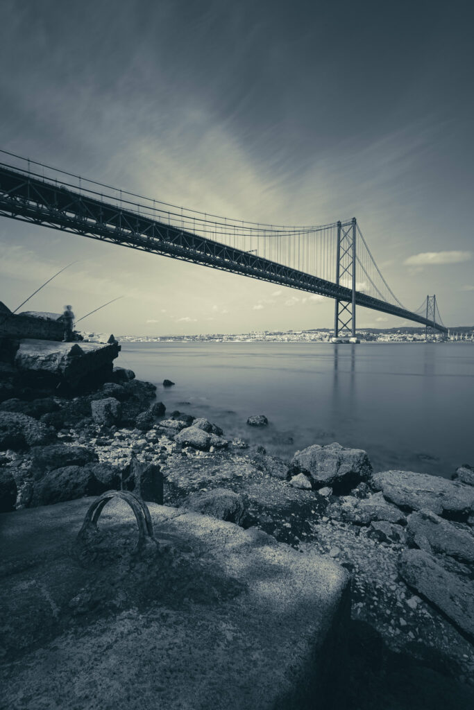 Serene riverside with smooth stones majestic bridge and distant city skyline in monochrome tones Wallpaper