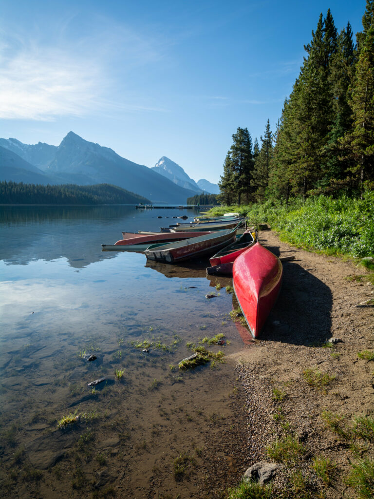 Colorful boats on calm river shore with lush trees mountains reflection and clear blue sky wallpaper