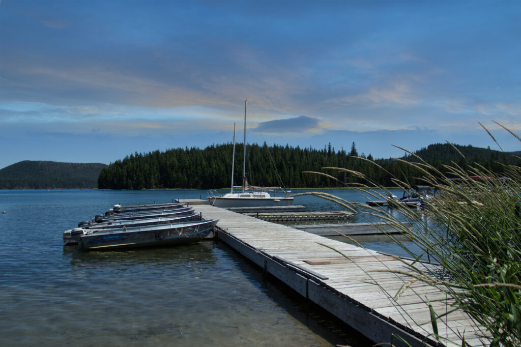 Peaceful riverside wallpaper with wooden pier boats and sailboat under clear blue sky