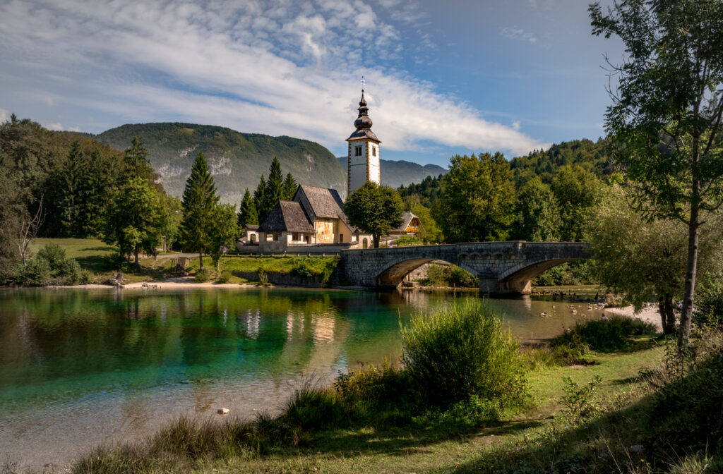 Tranquil riverside with stone bridge church tower lush green hills clear water wallpaper background