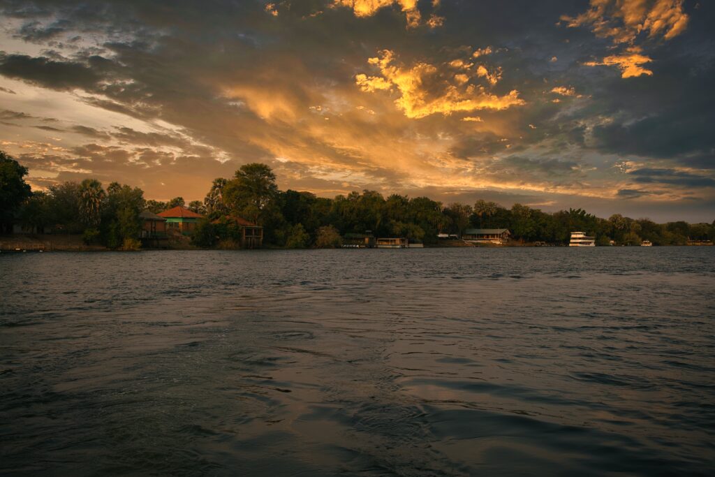 Sunset riverside wallpaper with warm glow reflecting on water and cozy houses by lush trees