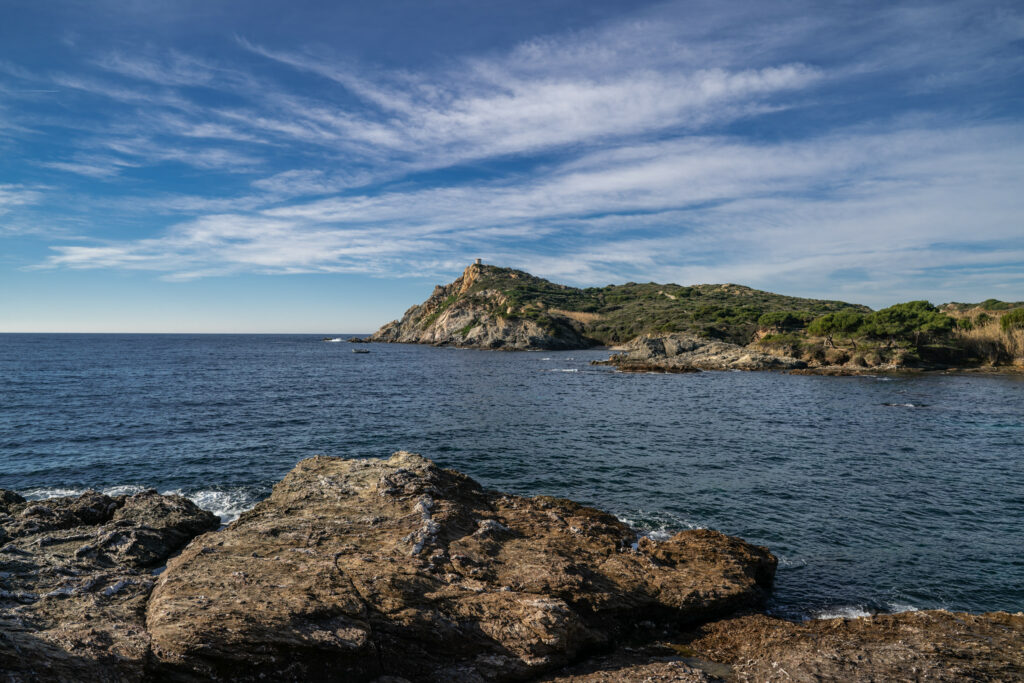 Rugged rocky shoreline with textured blocks cliffs and blue sea under wispy cloud sky wallpaper