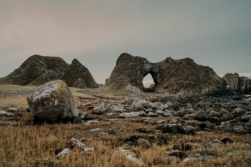 Serene natural landscape with rugged rocks grassy plain and rolling hills in soft earthy tones Wallpaper