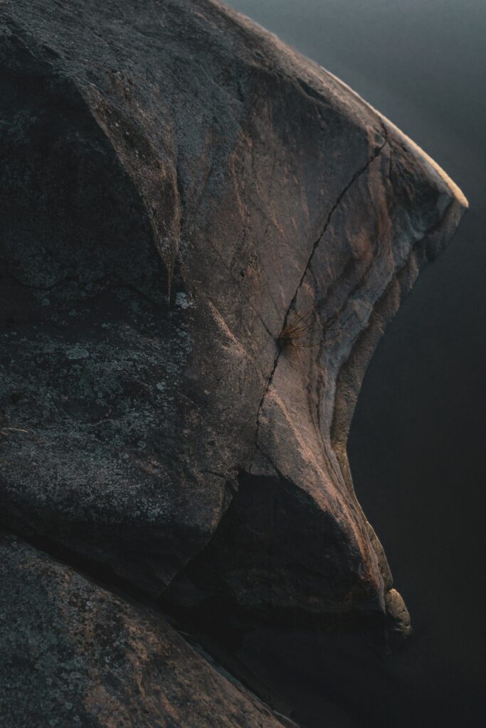 Close-up of rugged stone with deep cracks by calm coastal water textured natural wallpaper background