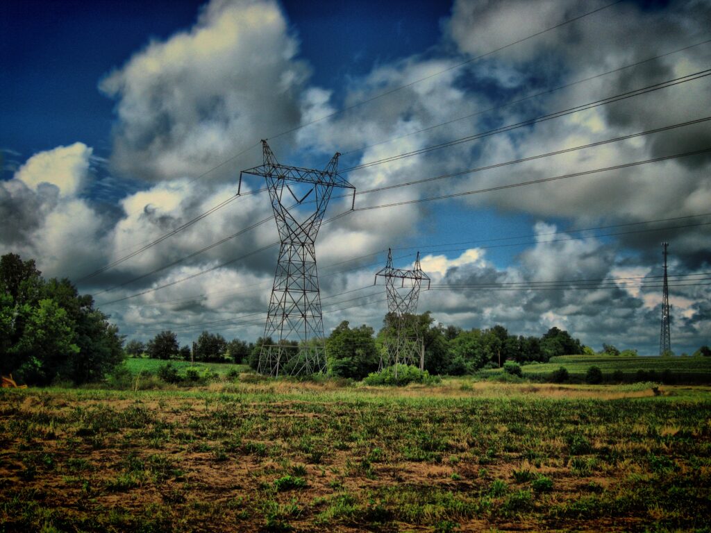 Tranquil rural landscape with open field tall poles wires dramatic clouds and green trees wallpaper