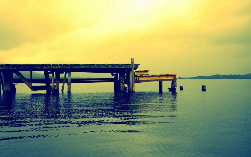 Rustic wooden pier over calm lake with gentle ripples and warm golden light at sunset wallpaper
