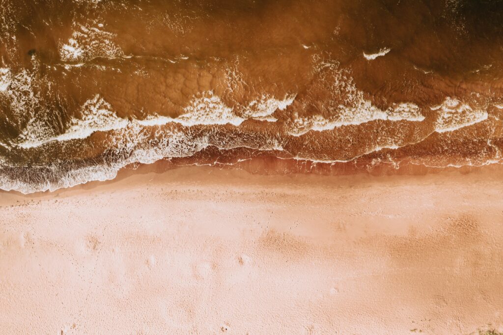 Aerial view of sandy coast with gentle waves meeting shore tranquil beach wallpaper background