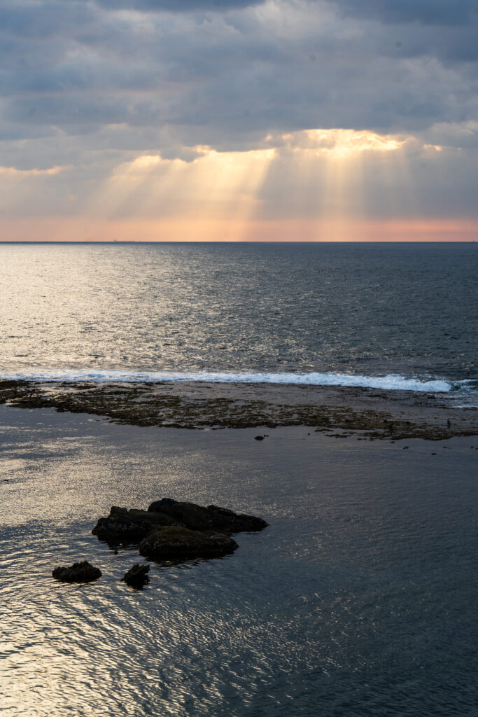 Aerial view of tranquil sea with small island golden sunrays through clouds serene nature wallpaper