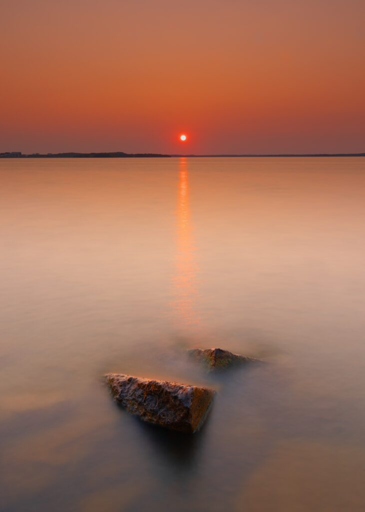 Tranquil sea sunset wallpaper with glowing orange skies calm waters rocky coast serene view
