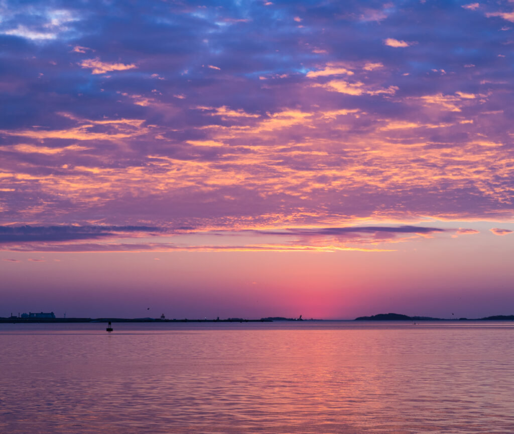 Tranquil sea at sunset with pink purple orange sky and calm reflective water wallpaper background
