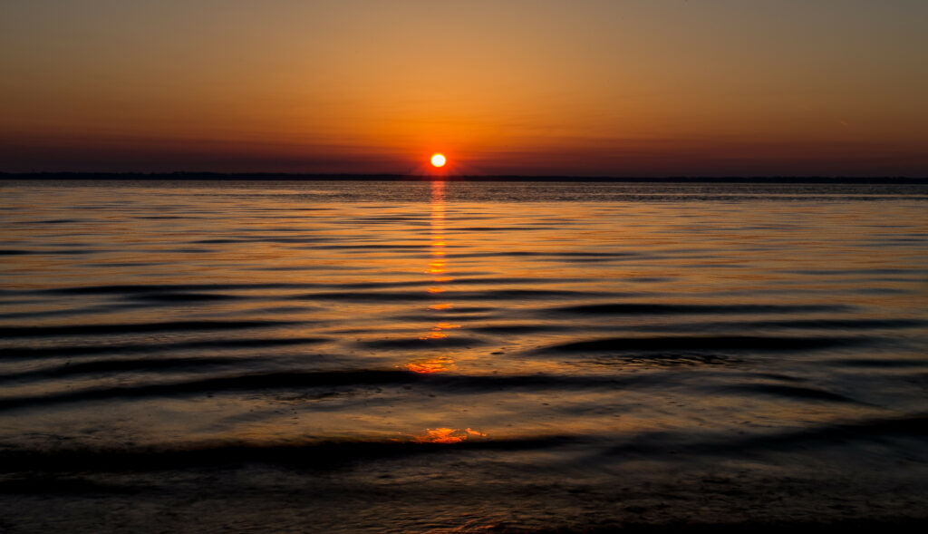 Serene sea at dusk with gentle waves reflecting vibrant orange and gold sunset hues wallpaper