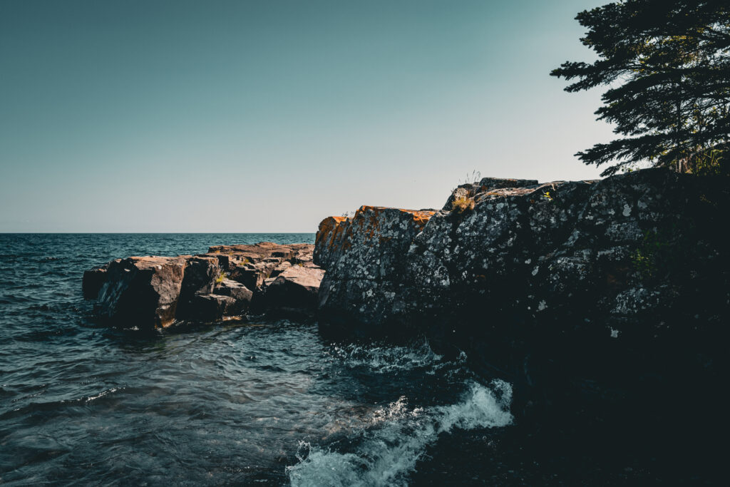 Rugged rocky coastline with textured cliffs and calm sea under clear blue sky nature wallpaper background