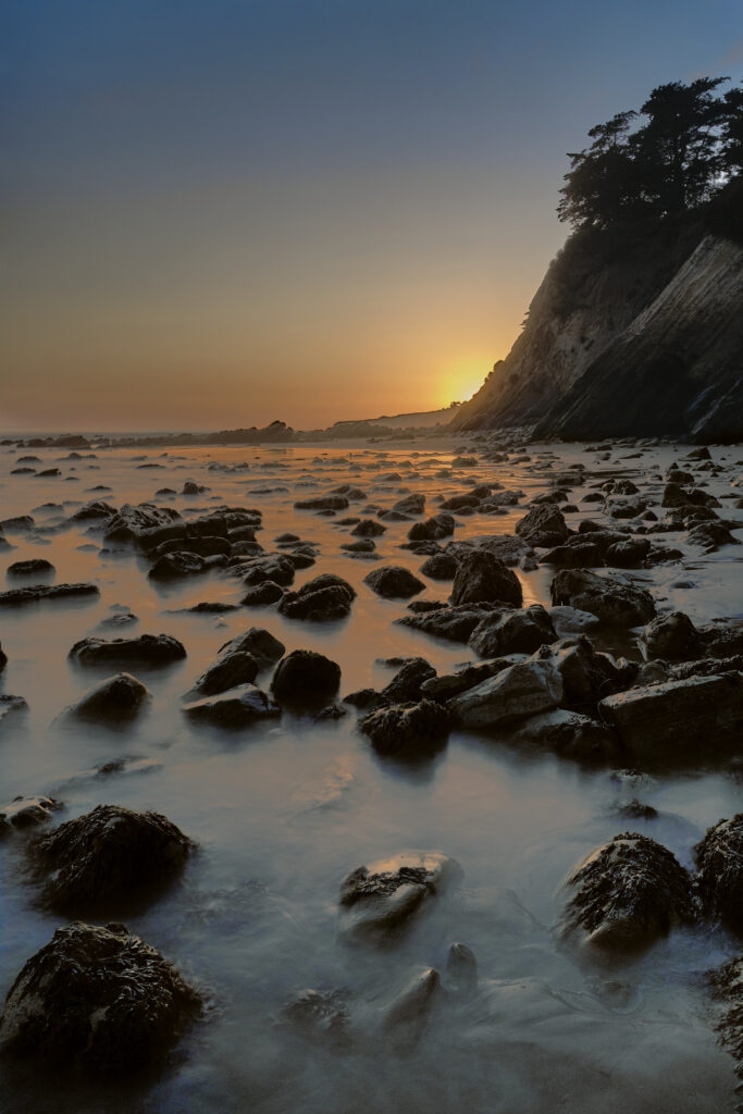 Tranquil seascape wallpaper with rugged shoreline rocks warm sunset glow calm water cliff trees
