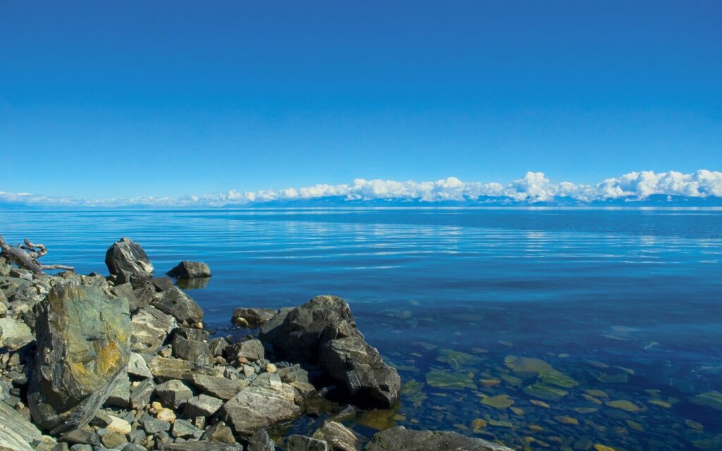 Tranquil seascape wallpaper with clear blue water rugged rocks and fluffy clouds in vast sky