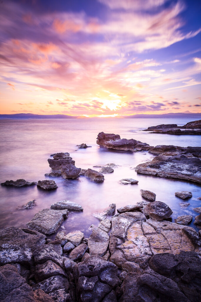 Tranquil seascape wallpaper with rugged stones calm water and vibrant purple gold sunset sky