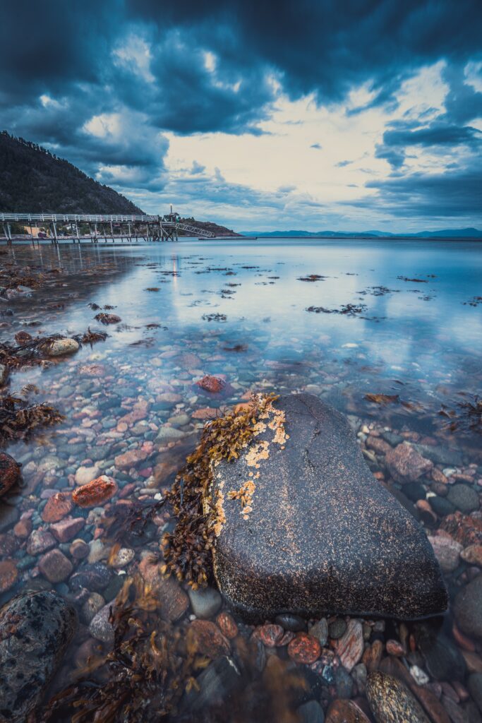 Dramatic seascape wallpaper with smooth pebbles large stone calm sea and moody cloudy sky