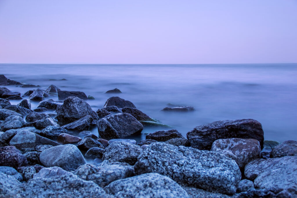 Tranquil seascape wallpaper with foggy calm blue waters and rugged stones in foreground