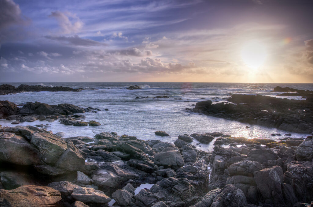Serene coastal wallpaper with rugged stones soft waves vivid sunset sky and gentle clouds