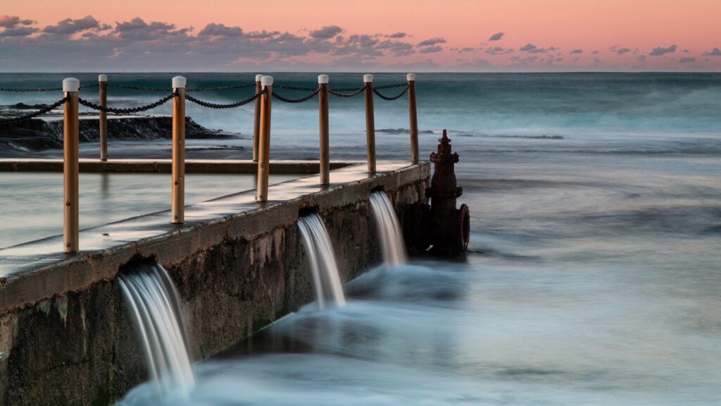 Tranquil sunset seaside pier with flowing water smooth sea pastel sky serene wallpaper background