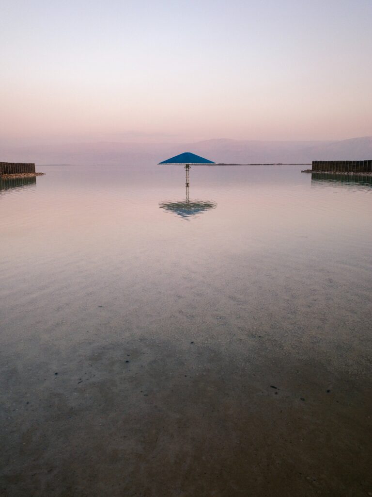 Serene seaside sunset with solitary blue umbrella reflecting in calm shallow water peaceful beach Wallpaper