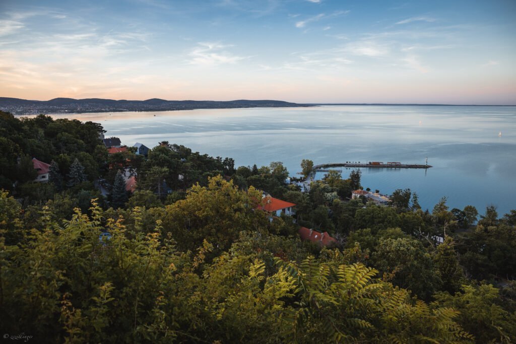 Tranquil seaside sunset with green trees charming houses and a long pier over calm blue sea wallpaper