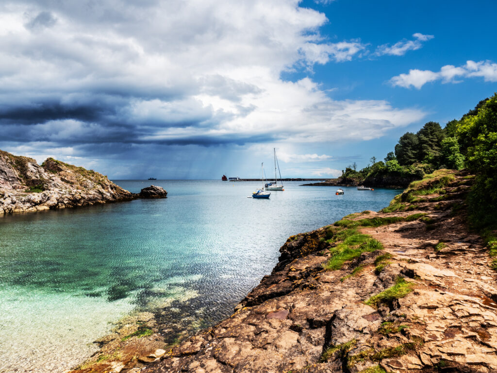 Seaside wallpaper with turquoise waters boats tall masts dramatic sky rocks and lush greenery