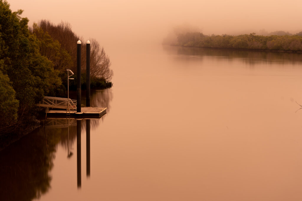 Serene sepia pier with tall pilings reflecting on still lake surrounded by misty trees wallpaper