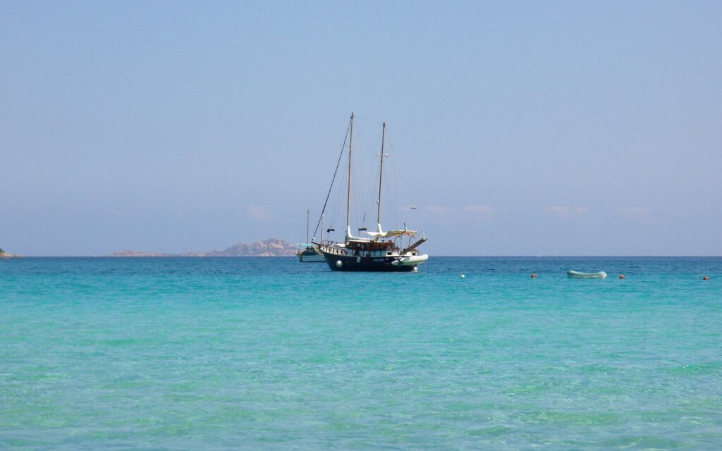 Tranquil ship on calm turquoise sea with clear sky and distant islands peaceful maritime scene Wallpaper