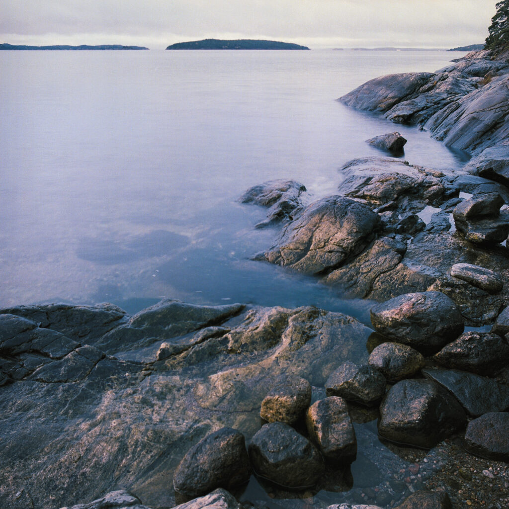 Tranquil shoreline with rugged stones smooth rocks calm sea and distant island in soft light Wallpaper