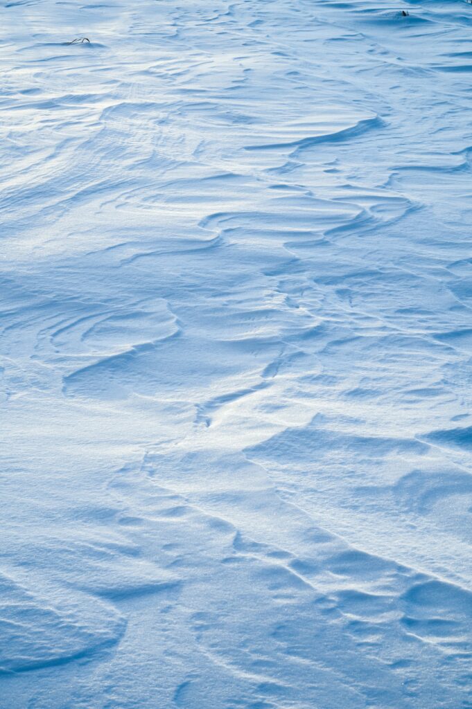 Snow-covered surface with soft white textures and gentle winter waves in cool blue tones background Wallpaper