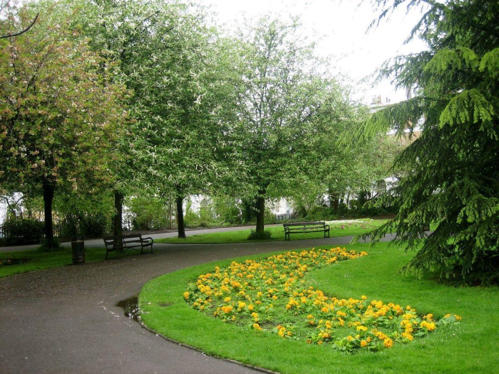 Spring park landscape with yellow flower bed and curving path amid lush green trees Wallpaper
