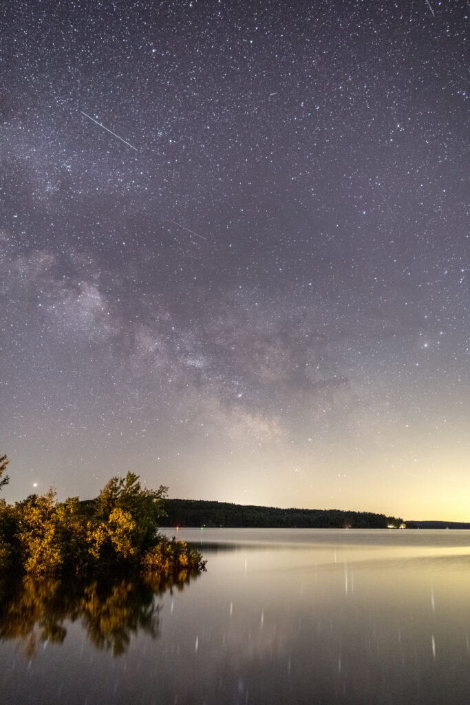 Tranquil lake reflects starry night sky with Milky Way and silhouetted trees at horizon Wallpaper