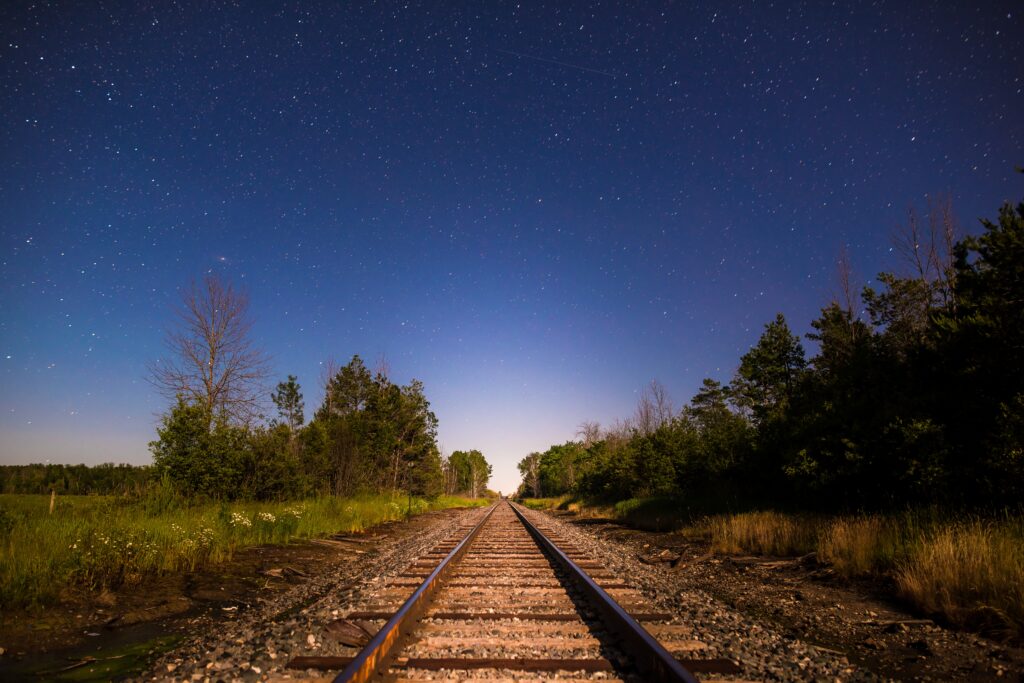Tranquil railway through lush forest under starry night sky in realistic immersive wallpaper background