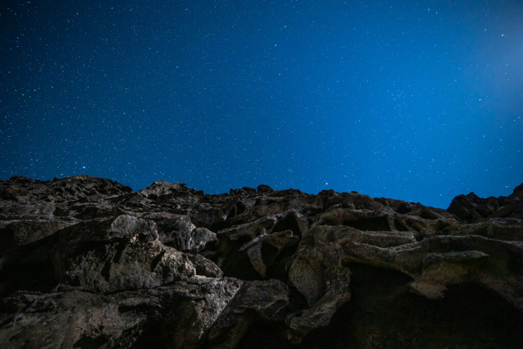 Rugged rock silhouettes under a starry deep blue night sky wallpaper background serene cosmic view