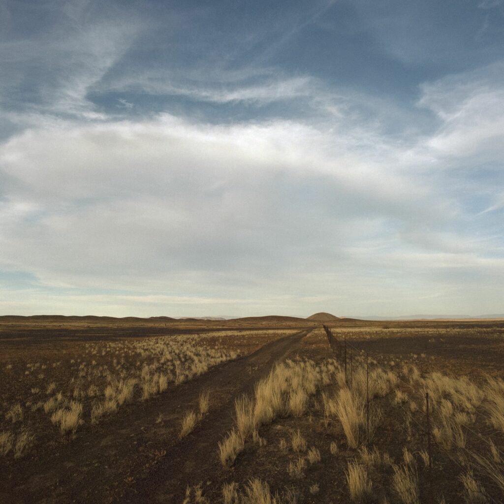 Tranquil steppe landscape with rolling hills golden grass rustic fence under cloudy sky wallpaper