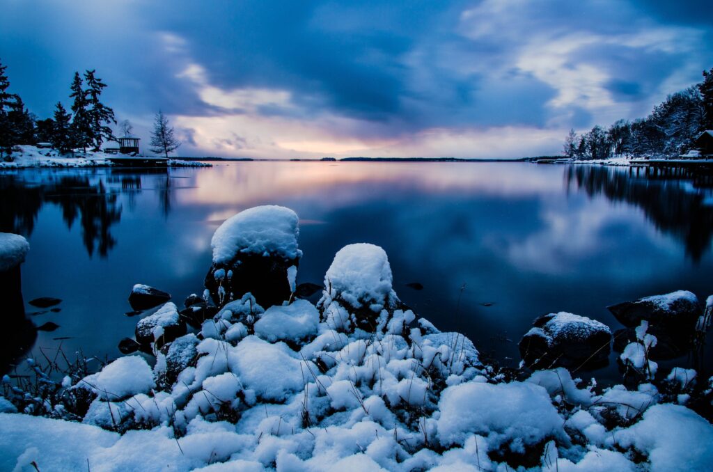 Tranquil winter evening in Stockholm with snow-covered rocks calm water and purple blue sky Wallpaper