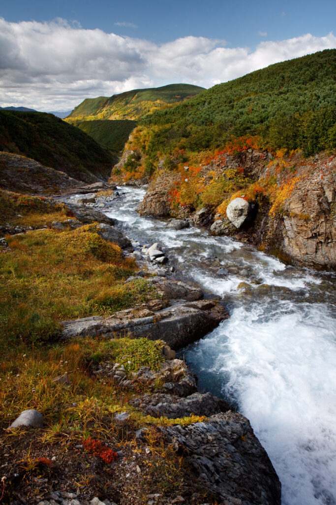 Clear stream flowing over stones with green hills and blue sky peaceful nature wallpaper background