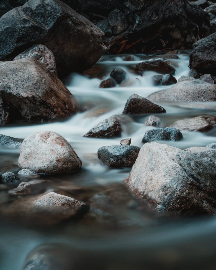 Serene stream flowing over smooth stones with rugged rocks in a tranquil natural setting wallpaper background