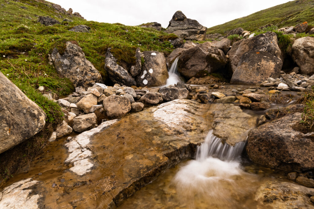 Serene stream flowing over smooth stones surrounded by lush green hills nature wallpaper background