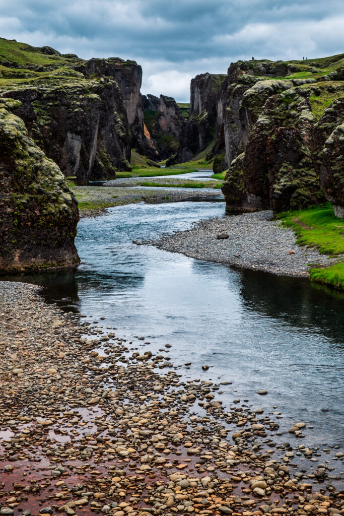 Tranquil stream flowing through lush green cliffs in dramatic gorge with smooth pebble riverbed Wallpaper