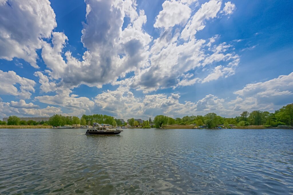 Boat gliding on Berlin Köpenick river under vibrant blue sky with clouds and lush green trees Wallpaper