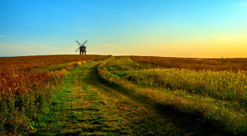 Tranquil summer countryside with winding path grassy field and classic windmill at sunset Wallpaper