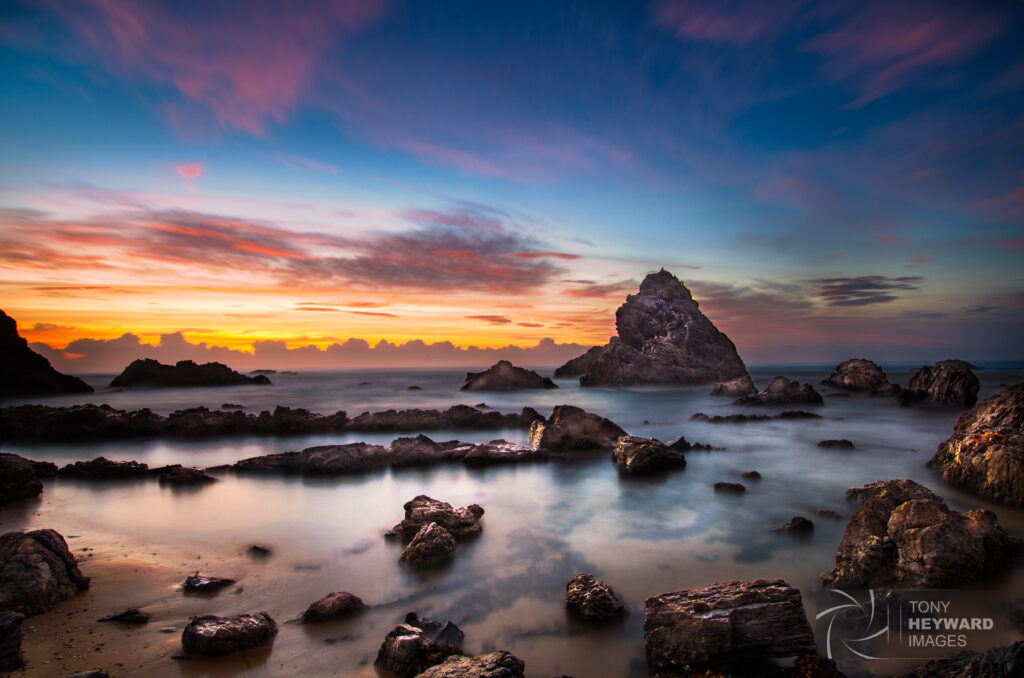 Tranquil sunrise over sea with rugged rocks golden light and wispy clouds coastal wallpaper background