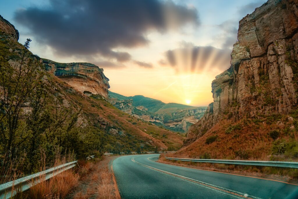 Winding road through rocky cliffs bathed in golden sunrise light over rugged landscape wallpaper